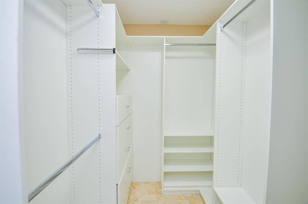 Primary walk-in closet features ample storage with multiple hanging rods, shelving units, and drawers, all in a clean, white finish.