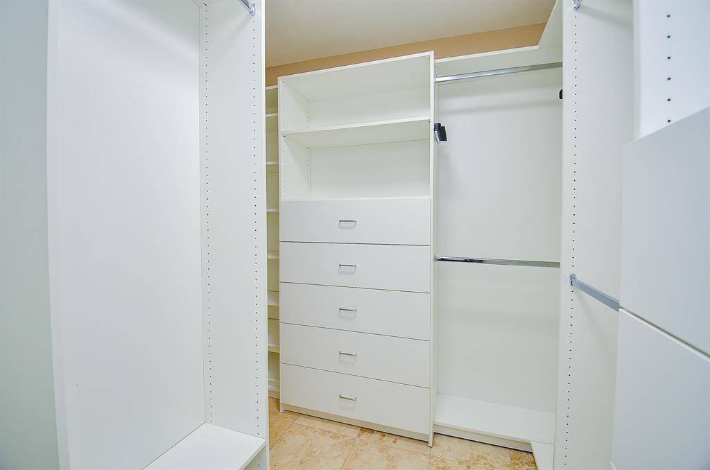 Adjacent to primary is the spacious walk-in closet featuring white shelving, multiple drawers, and ample hanging space. Ideal for organized storage.