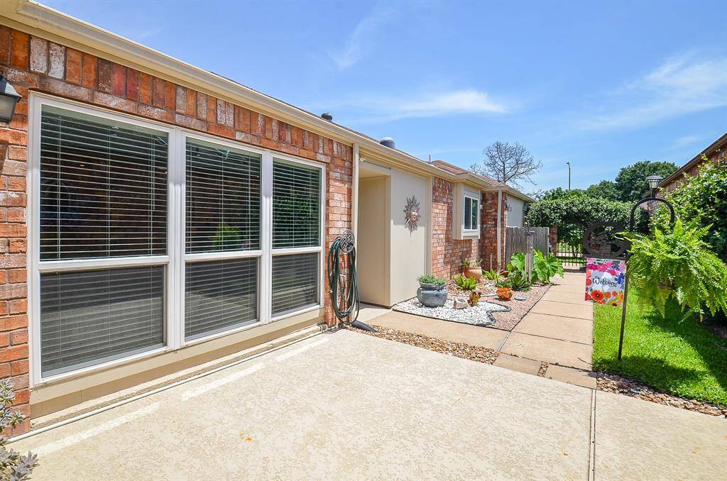 Immaculate.  Brick exterior with large windows and a welcoming pathway. The yard is well-maintained, featuring decorative plants and a cheerful "Welcome" sign. Ideal for enjoying outdoor space and natural light.