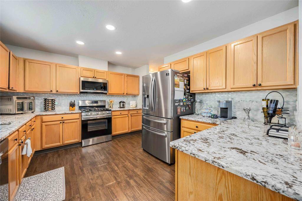 Spacious kitchen with warm wood cabinetry, stainless steel appliances, and granite countertops. It features ample storage, a modern backsplash, and a cozy atmosphere with recessed lighting and hardwood floors.