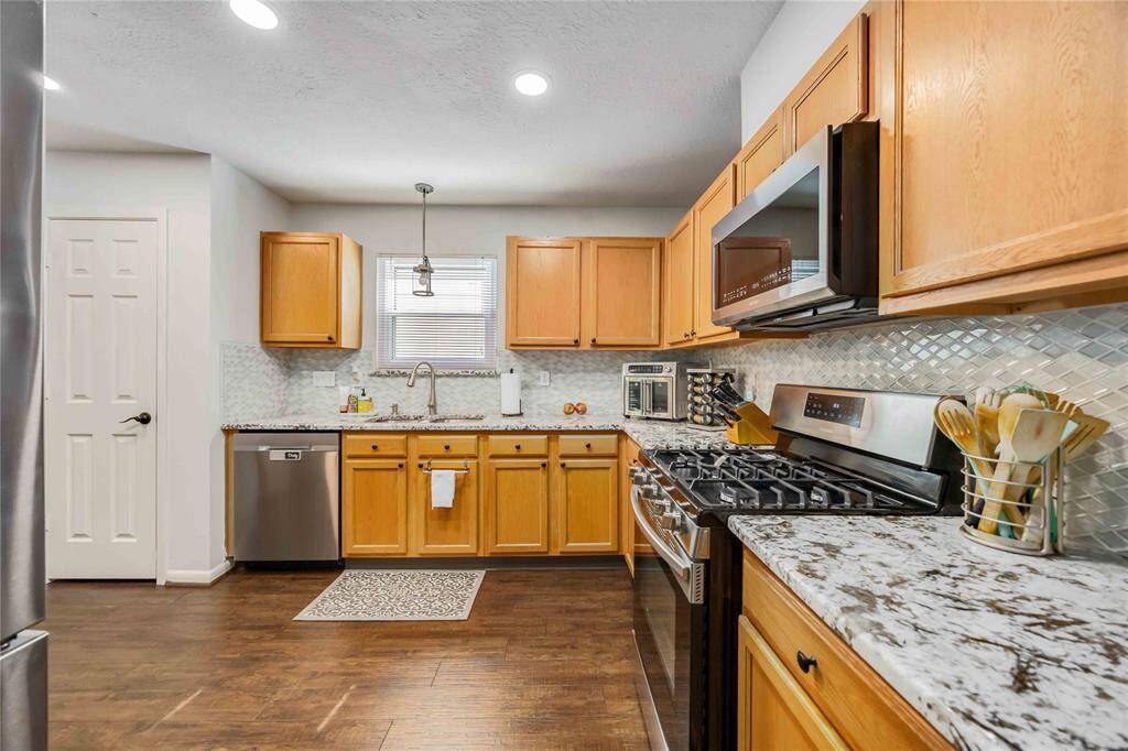 Modern kitchen with stainless steel appliances, granite countertops, and light wood cabinetry. Features a sleek tile backsplash, recessed lighting, and dark hardwood floors for a warm, inviting feel.