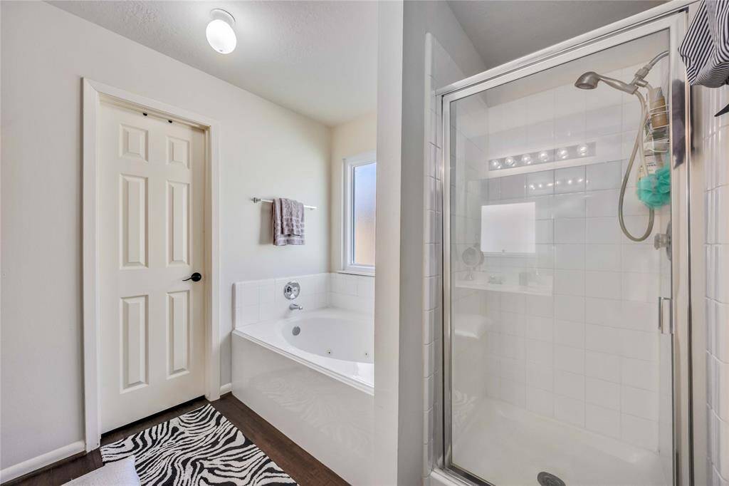 This bathroom features a spacious glass-enclosed shower, a separate bathtub, and a modern sink area. Natural light fills the room through a window, complementing the clean, neutral decor.