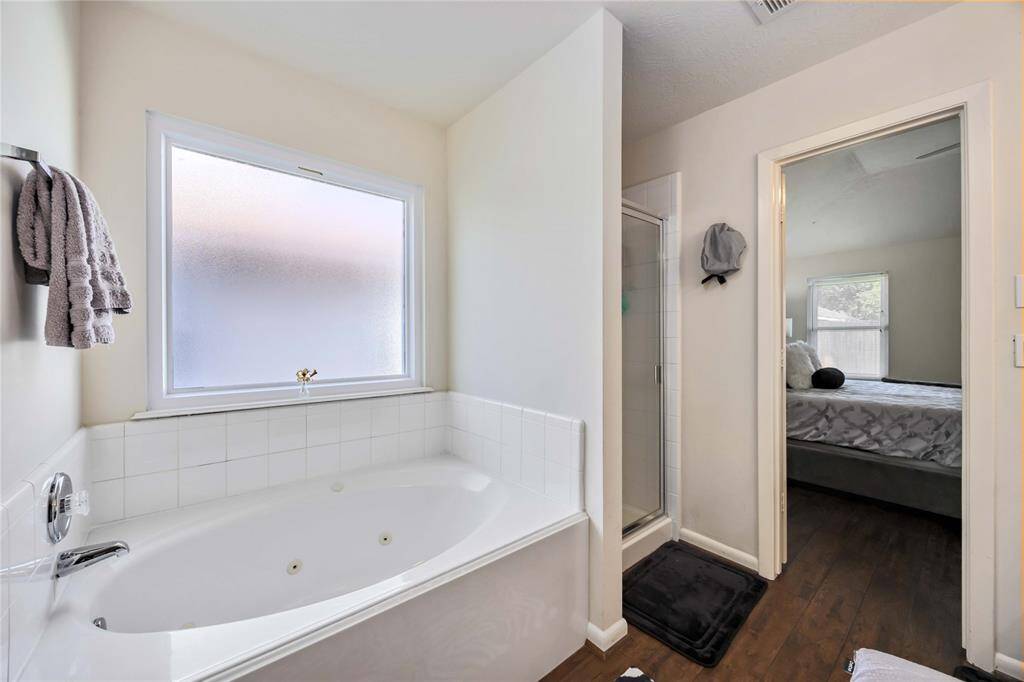 This photo shows a bright bathroom with a large corner bathtub, a separate shower, and an adjoining bedroom. Natural light enters through a frosted window, creating a welcoming atmosphere.