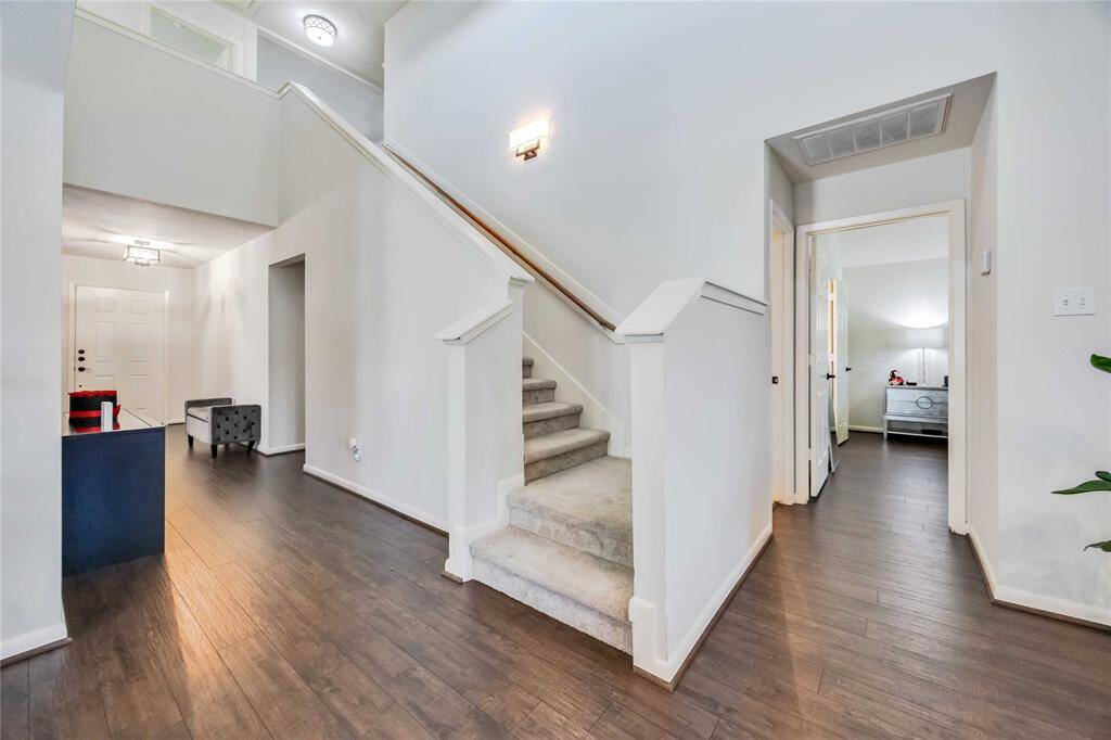 This photo showcases a bright, welcoming entryway with a staircase leading to the second floor. It features light-colored walls, hardwood flooring, and modern light fixtures. The hallway leads to additional rooms, offering a spacious and open feel.