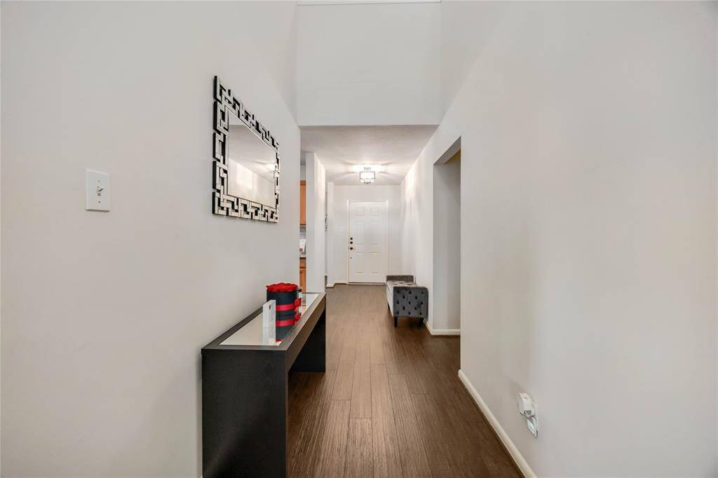 This photo shows a bright, welcoming hallway with hardwood floors, a modern console table, a decorative mirror, and a cozy bench by the entrance.