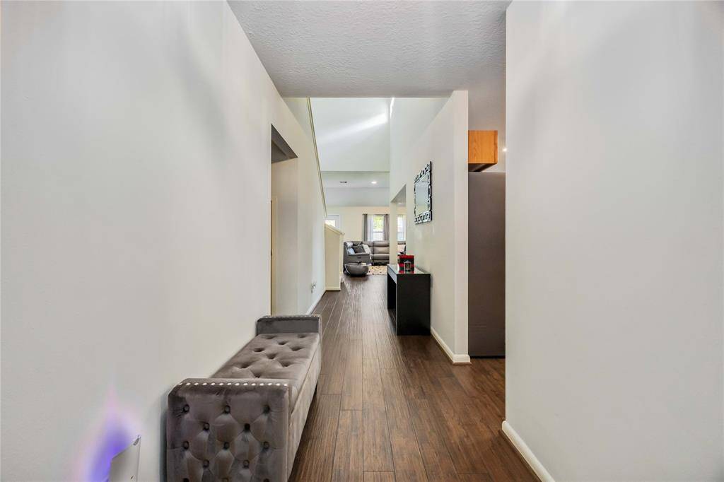 This photo showcases a modern, well-lit hallway with hardwood flooring, leading to an open living area. The space features a sleek, contemporary design with neutral walls and stylish furnishings, creating a welcoming atmosphere.