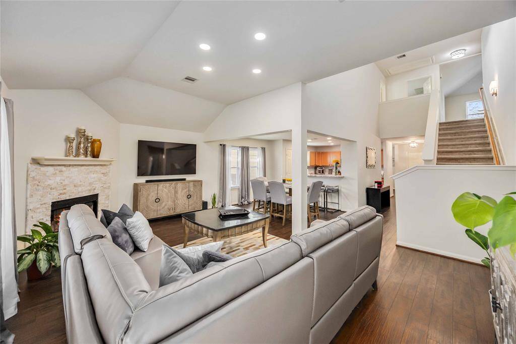 This inviting living room features high ceilings, a cozy fireplace, and an open layout leading to a modern kitchen. The space is well-lit with recessed lighting and offers a stylish, comfortable seating area. A staircase leads to the upper level, adding to the home's spacious feel.