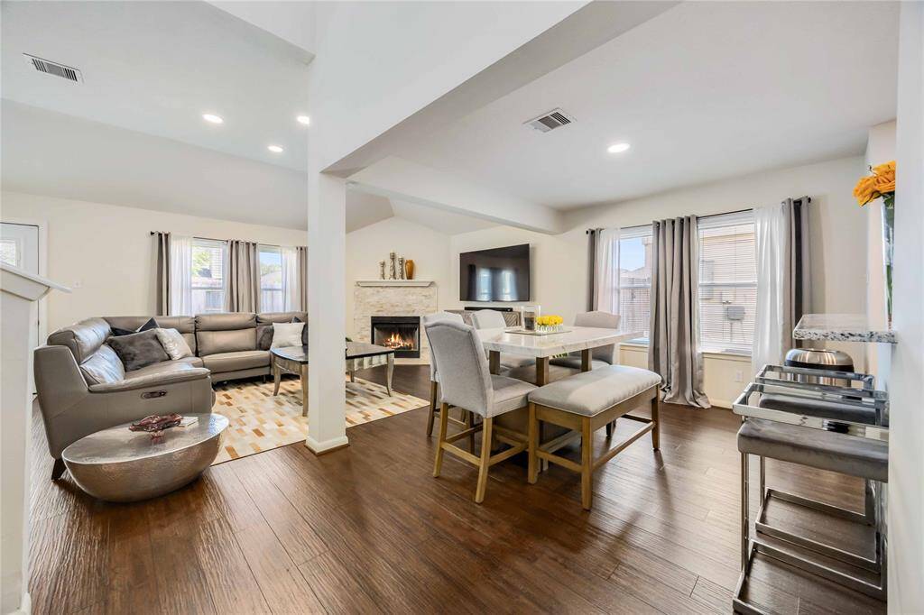 This inviting open-concept living space features a cozy seating area with a fireplace, modern dining area, and large windows for natural light, all enhanced by warm wood flooring and neutral tones.