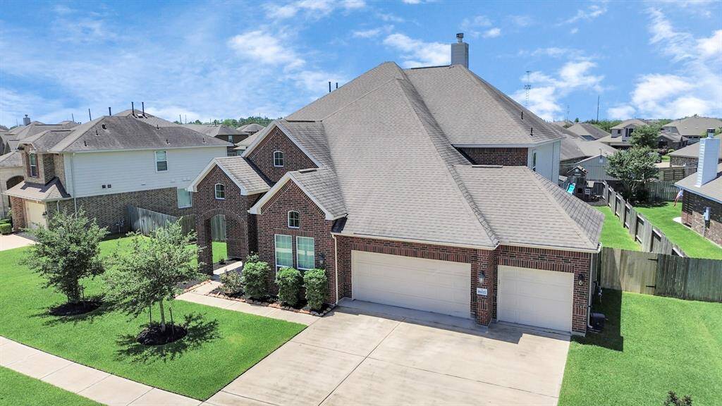 This spacious two-story brick home features a three-car garage and a well-maintained front lawn. It is situated in a suburban neighborhood, offering ample driveway space and a fenced backyard for privacy.
