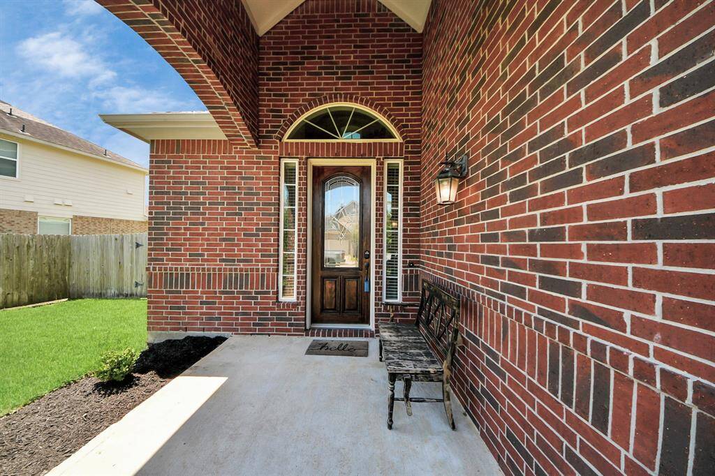 Charming front entry with a red brick exterior and an arched doorway. Features a welcoming porch with a decorative bench and a classic lantern-style light fixture.