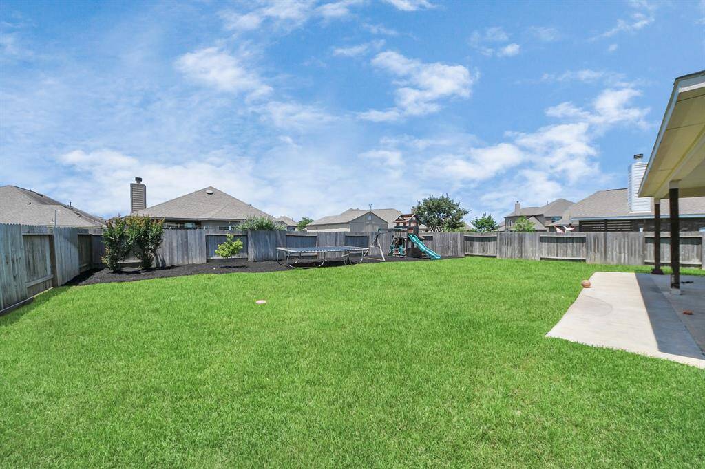 Spacious backyard with lush green lawn, a swing set, and fenced perimeter, perfect for family activities and outdoor entertaining.