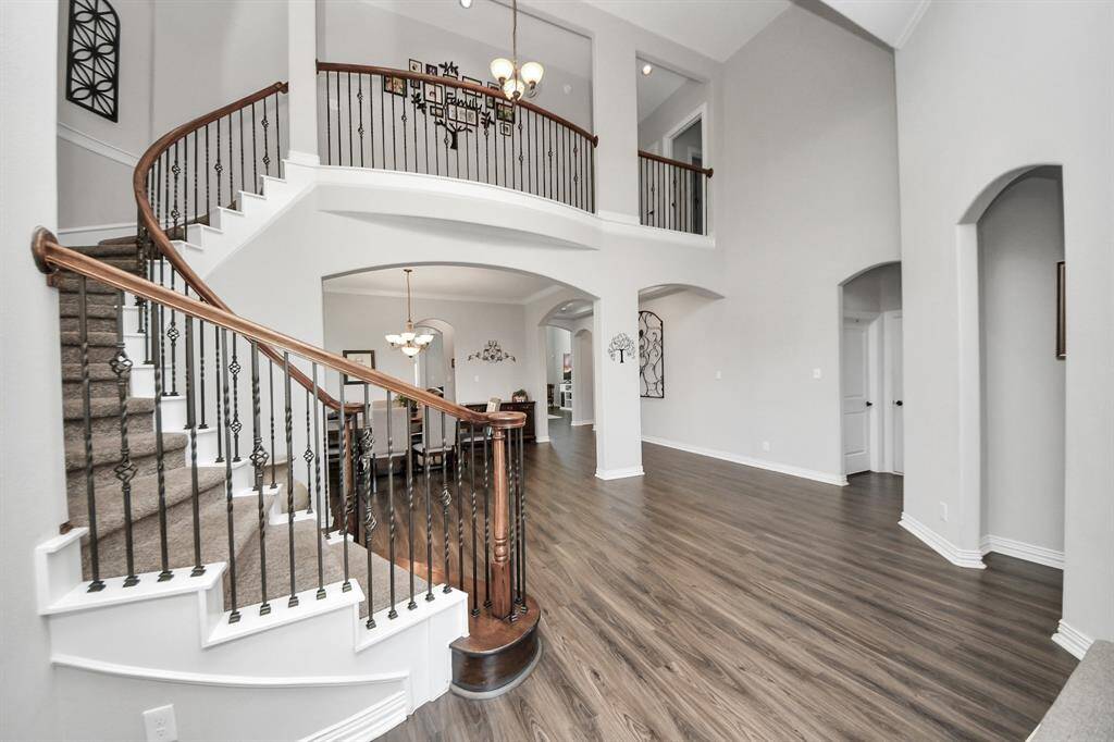 This photo showcases a spacious, elegant entryway with high ceilings and a sweeping curved staircase featuring dark wood railings and iron balusters. The open floor plan includes beautiful flooring and ample natural light, creating a welcoming atmosphere.