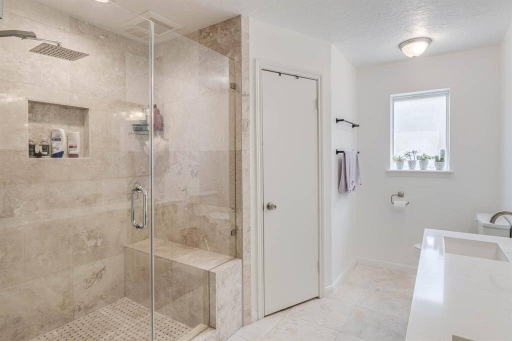 "The luxurious primary suite includes a spa-like bathroom with a sleek, frameless glass walk-in shower and elegant tile finishes.
