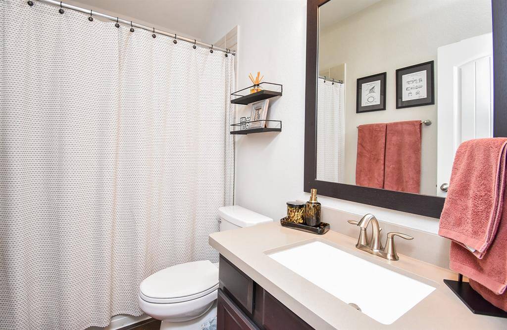 Full bath has a tub shower combo. Framed mirror accents the vanity.