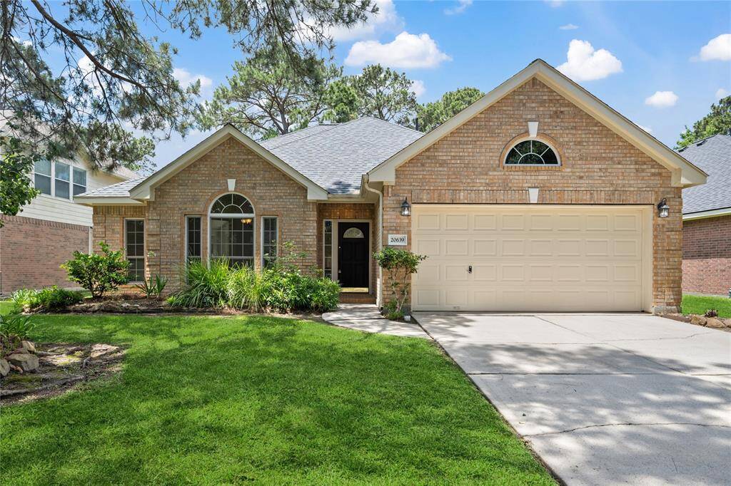Charming single-story brick home with a well-maintained front yard and a two-car garage. The property features large arched windows and a welcoming entrance, surrounded by lush greenery.