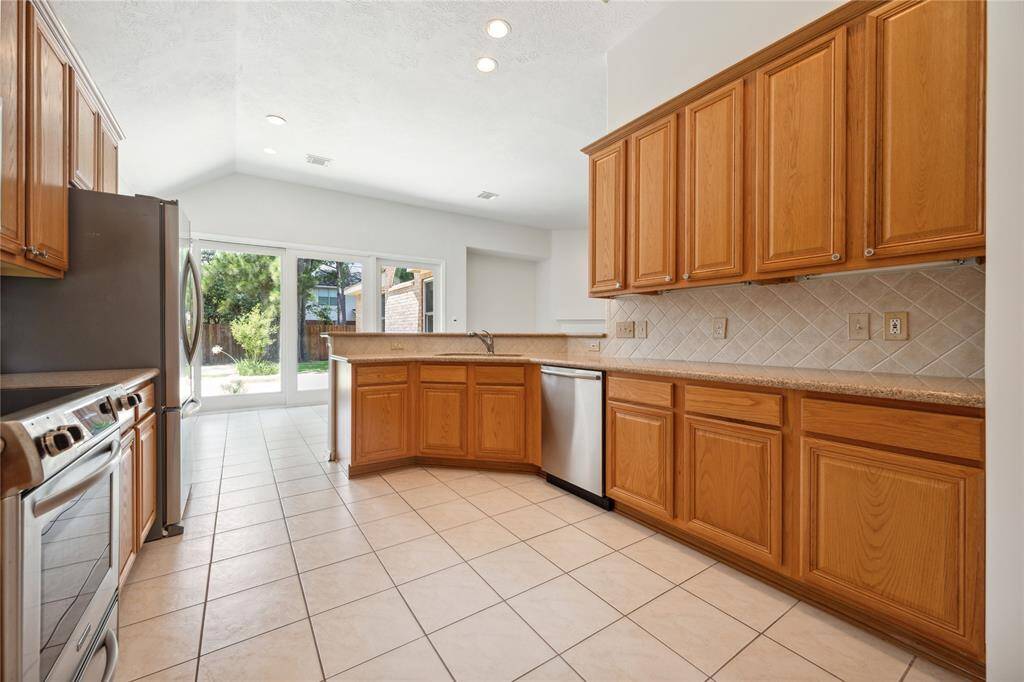 Bright kitchen with ample natural light, featuring wooden cabinets, tiled floors, stainless steel appliances, and a view of the backyard through large glass doors.