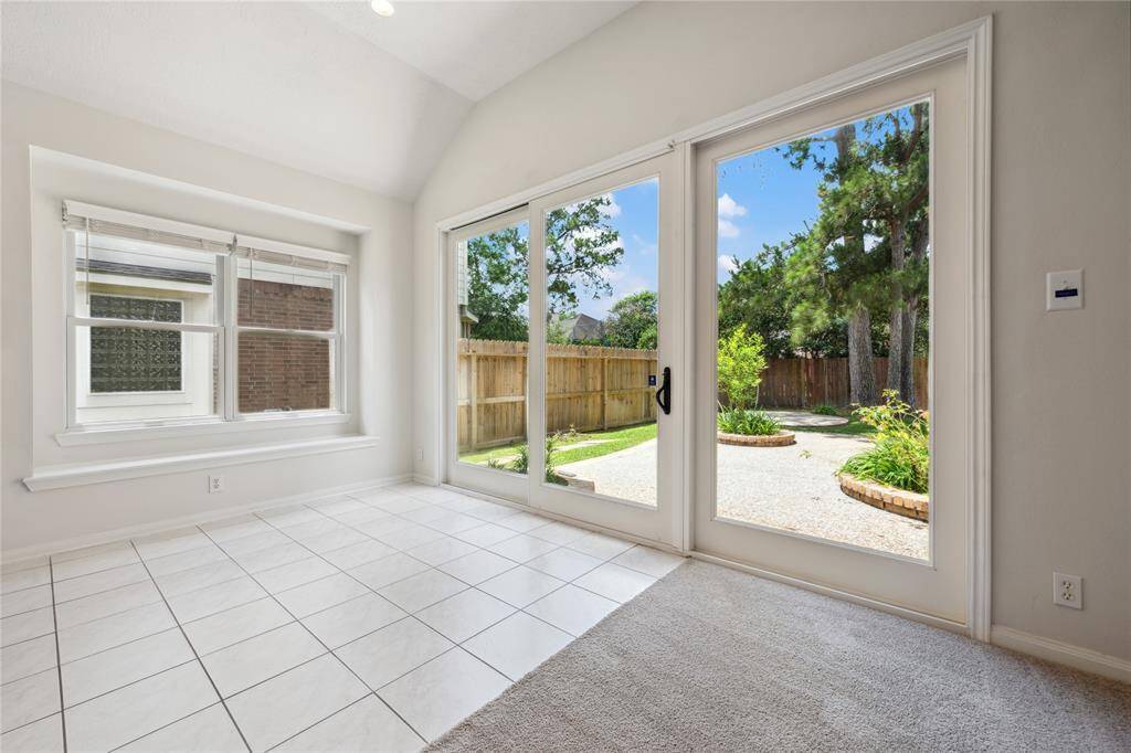 Bright room with large windows and sliding doors leading to a landscaped backyard. Features tiled flooring, neutral walls, and abundant natural light, creating a welcoming indoor-outdoor living space.