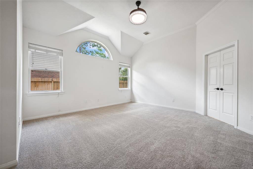This room features neutral-colored walls and carpet, creating a bright and airy atmosphere. It has a high ceiling with a modern light fixture and two large windows, including a decorative arched window, allowing plenty of natural light. A double-door closet offers storage space.