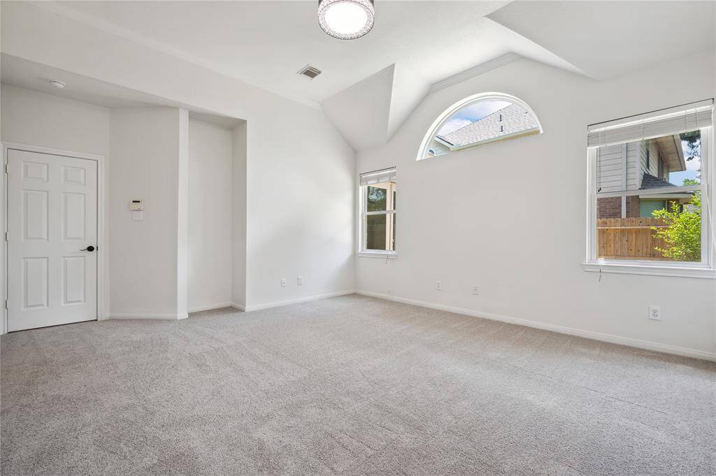 Bright, spacious room with vaulted ceiling, neutral carpet, and ample natural light from large windows. Ideal for a bedroom or home office.
