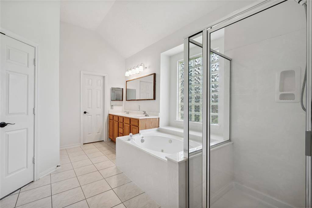 This spacious bathroom features a walk-in shower, a separate soaking tub, a large vanity with ample storage, and abundant natural light from a frosted window.