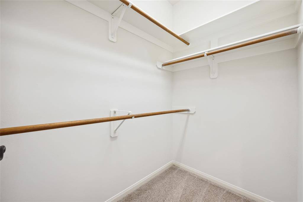 This is a spacious walk-in closet with multiple wooden hanging rods and beige carpet, providing ample storage space.