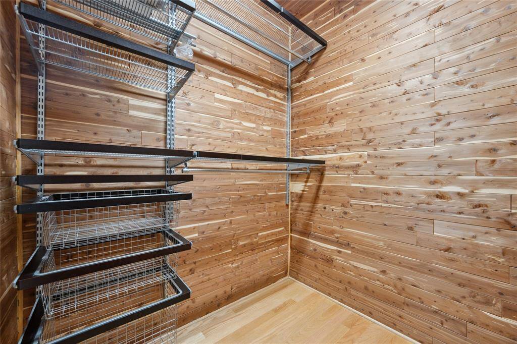 This photo shows a spacious walk-in closet with warm wooden walls and multiple metal shelving units for organized storage.
