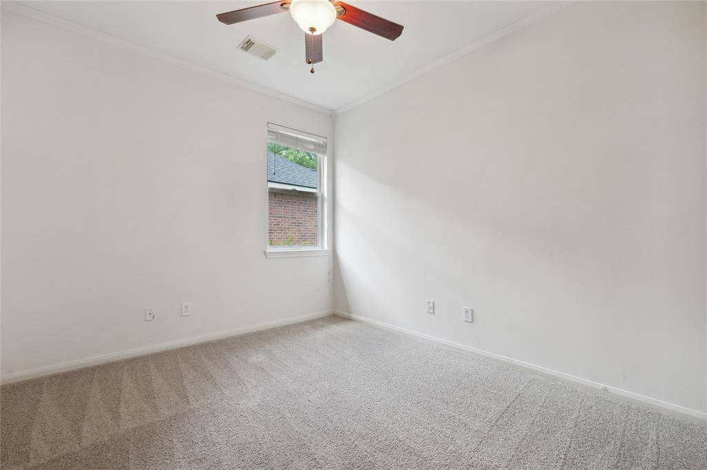 This room features neutral walls and carpet, a ceiling fan, and a window providing natural light. Perfect as a bedroom or office.