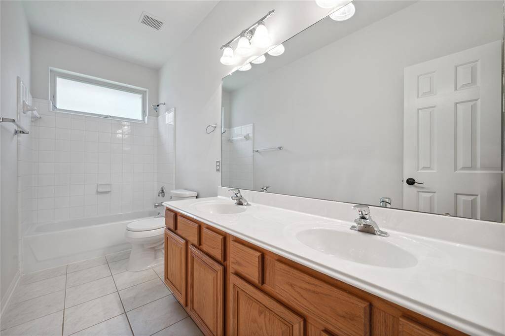 This bathroom features a clean, bright design with a double sink vanity, large mirror, and wood cabinets. It includes a bathtub with a shower, tiled walls, and a frosted window for natural light.