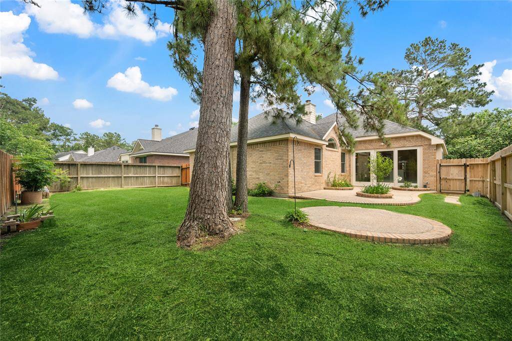 This photo showcases a spacious backyard with lush green grass, mature trees, and a brick patio area. The house features a brick exterior with large windows and a fenced yard, offering privacy and a great outdoor space for relaxation or entertaining.