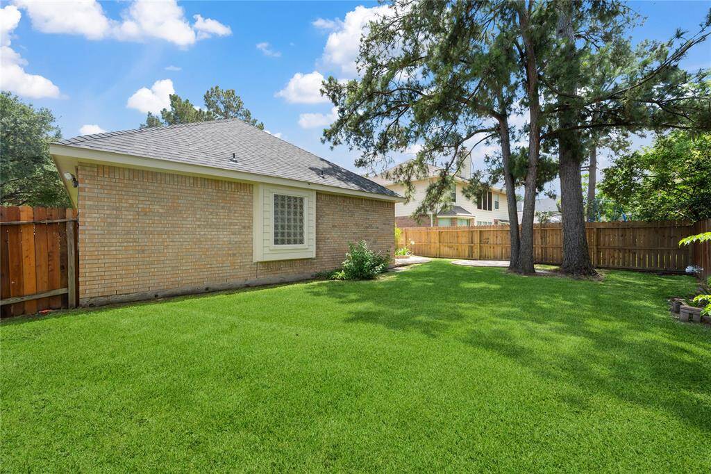 This photo showcases a spacious backyard with well-maintained grass, bordered by a wooden fence. It features mature trees providing shade and a side view of a brick house with a large window. Ideal for outdoor activities and relaxation.
