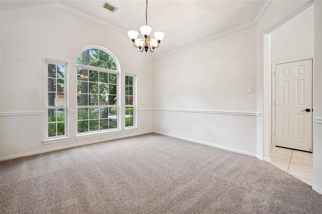 Bright room with a large arched window, soft carpet, and a classic chandelier. The neutral walls feature elegant chair and crown molding, and there's an adjoining doorway leading to a tiled area. Ideal for a dining or living space.