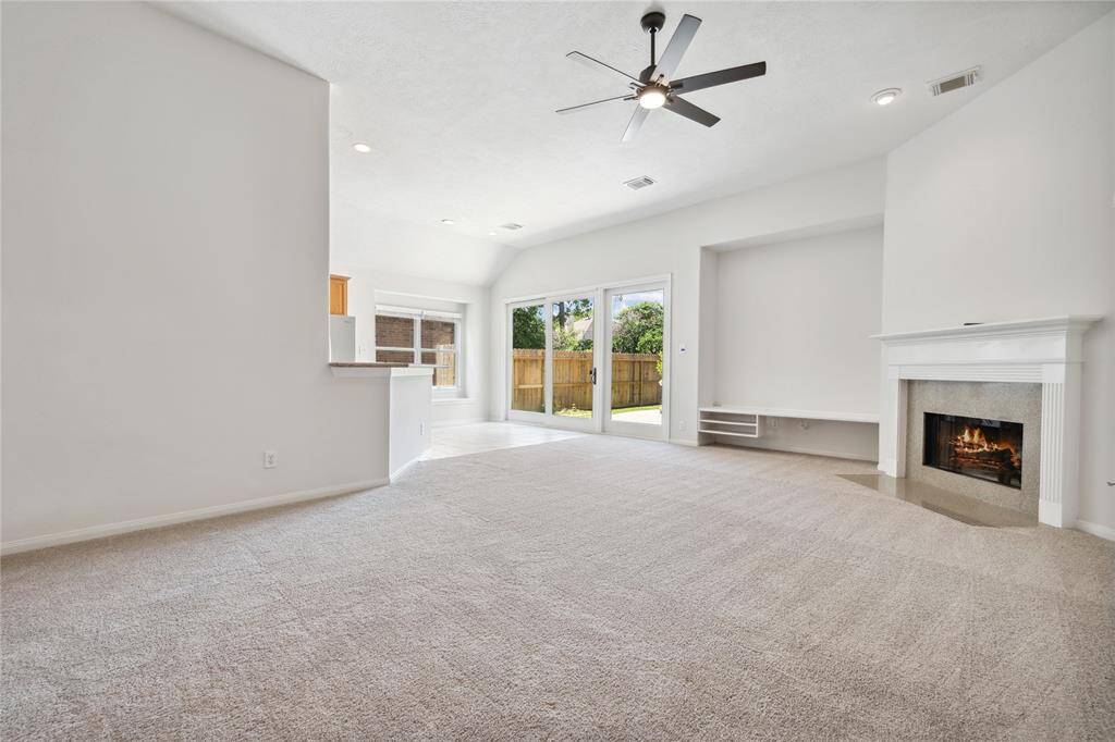Bright and spacious living area featuring a ceiling fan, cozy fireplace, and large sliding doors leading to a fenced backyard, offering plenty of natural light.
