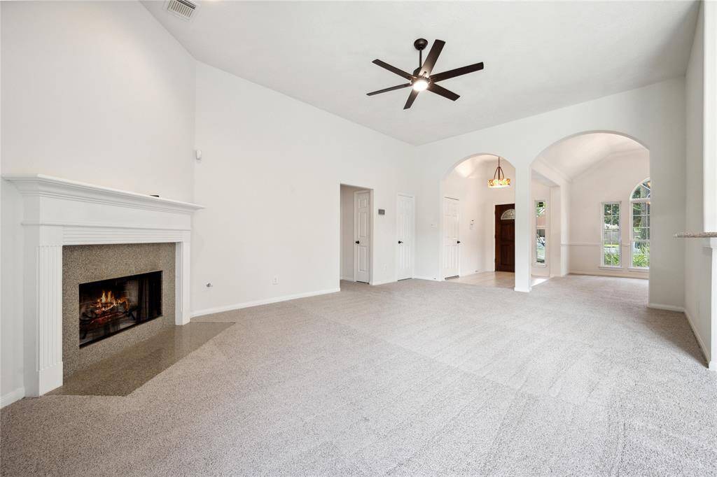This spacious living room features a cozy fireplace, high ceilings with a modern ceiling fan, and an open layout leading to a bright dining area with large arched windows. Ideal for comfortable living and entertaining.