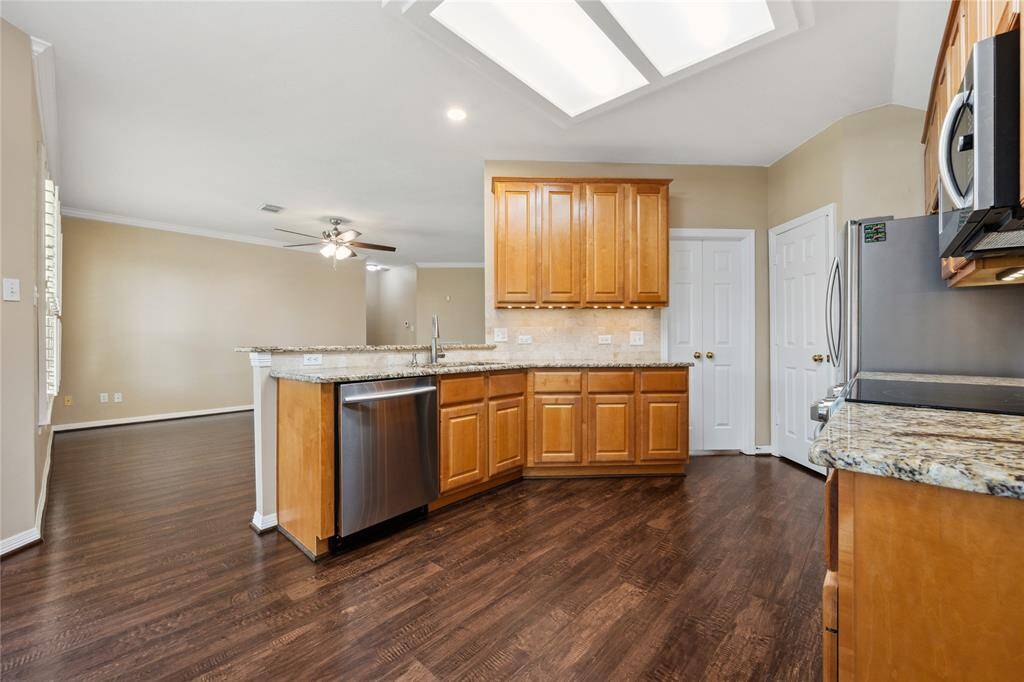 This kitchen boasts granite countertops, stainless steel appliances, and ample wooden cabinetry. It opens into a spacious living area with hardwood floors and a ceiling fan, providing a warm and inviting atmosphere.