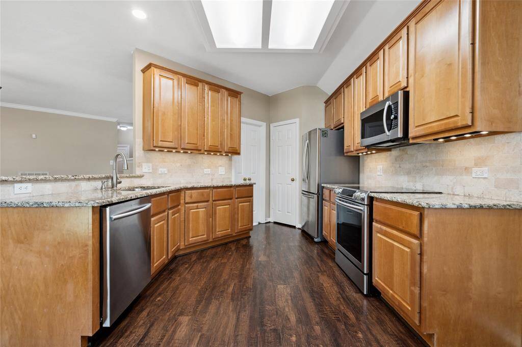 Spacious kitchen with warm wood cabinetry, granite countertops, and stainless steel appliances. Features a built-in microwave, dishwasher, and ample storage, all complemented by elegant wood flooring. Ideal for culinary enthusiasts.