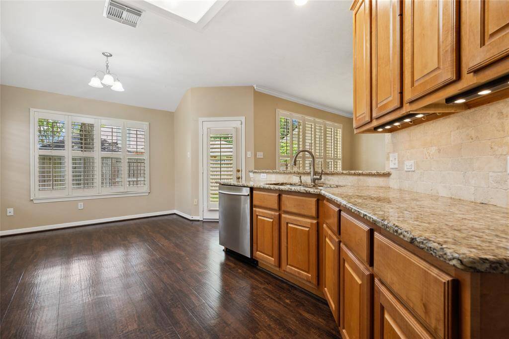 This photo showcases a bright kitchen and dining area with hardwood floors, wooden cabinets, granite countertops, and large windows with shutters, offering a warm and inviting atmosphere.