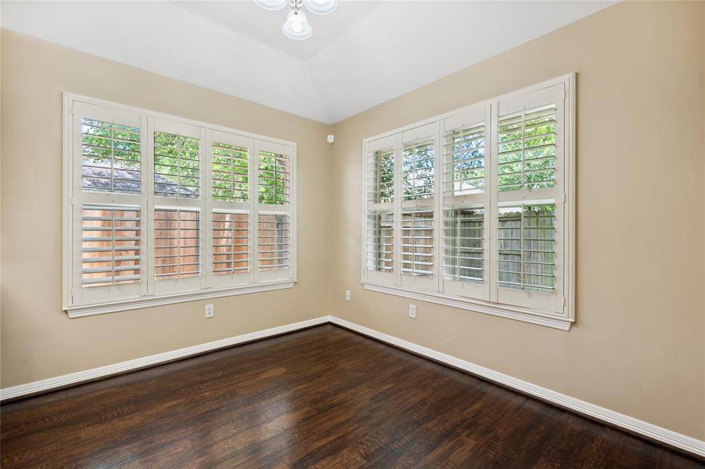 Bright room with large windows featuring white shutters, neutral walls, and dark wood  floors, creating a warm and inviting space.