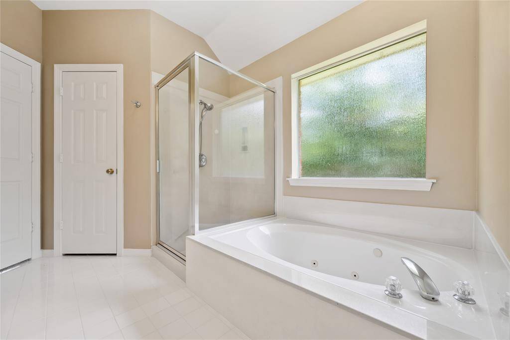 This bathroom features a spacious bathtub with jets, a separate glass-enclosed shower, and a large frosted window for natural light and privacy. The neutral color scheme adds a warm touch.