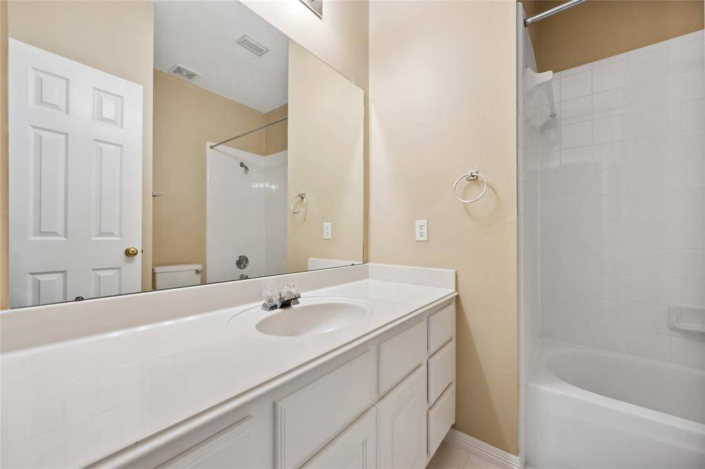 This bathroom features a clean, modern design with a large mirror, a spacious white vanity with ample storage, and a combination bathtub and shower. The neutral tones create a bright and inviting atmosphere.