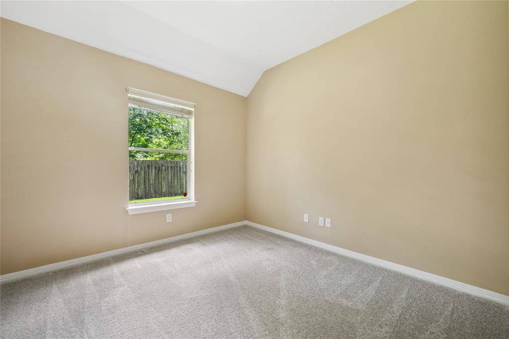 This room features neutral walls, a soft carpet, and a window overlooking a fenced yard, offering a cozy and serene atmosphere.