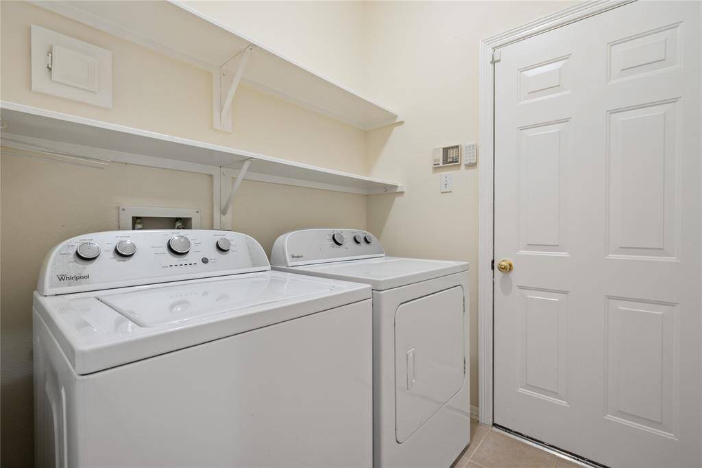Laundry room featuring a washer and dryer set with overhead shelving for storage. The room is well-lit with a neutral color scheme and includes a door for easy access to garage.