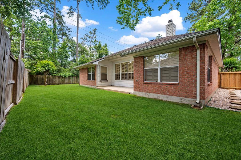 Charming backyard with lush green grass, a brick exterior, and a patio. Surrounded by a wooden fence and trees, offering privacy and a serene atmosphere. Perfect for outdoor relaxation and gatherings.