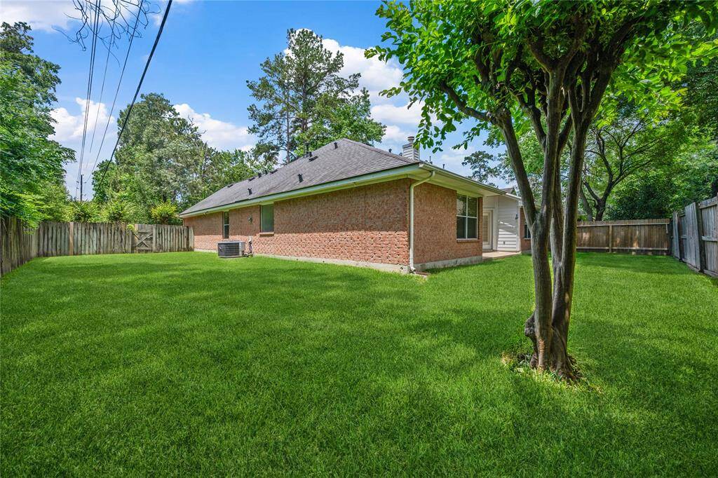 This photo showcases a spacious backyard with lush green grass, a mature tree, and a wooden fence surrounding a brick house. Ideal for outdoor activities and privacy.