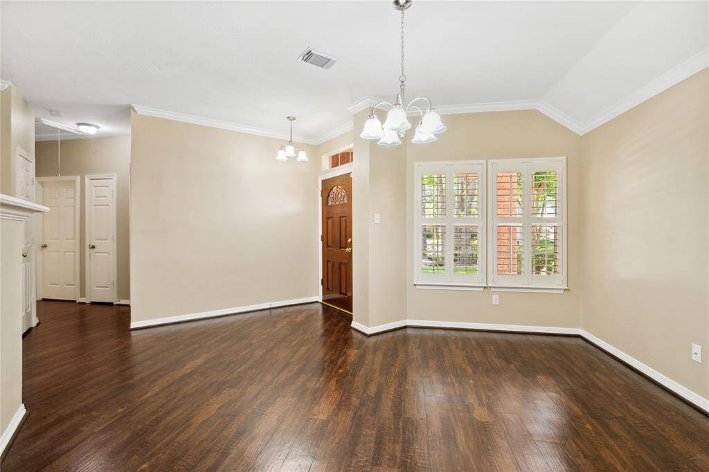 This dining room features warm wood floors, beige walls, and a chandelier. It has a wooden front door and windows with white shutters, offering a bright and welcoming entrance area.