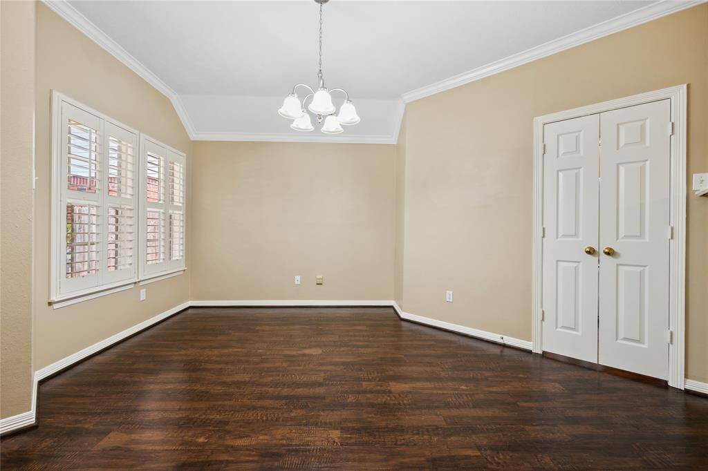 This is a bright, open dining room featuring wood floors, neutral walls, and a classic white double-door leading to the kitchen. Large windows with shutters provide ample natural light, and a central light fixture adds a touch of elegance. Perfect for a dining area or office space.