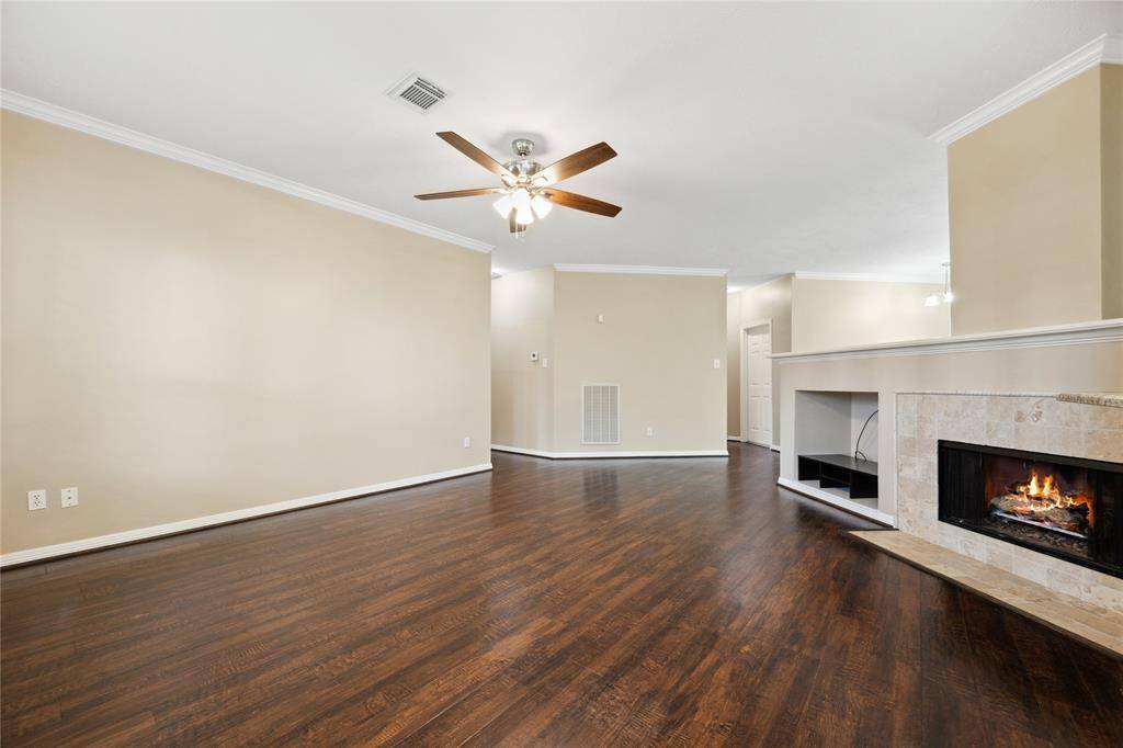 This spacious living room features elegant wood floors, a cozy fireplace, neutral walls, and a ceiling fan. The open layout is ideal for entertaining and offers plenty of natural light.