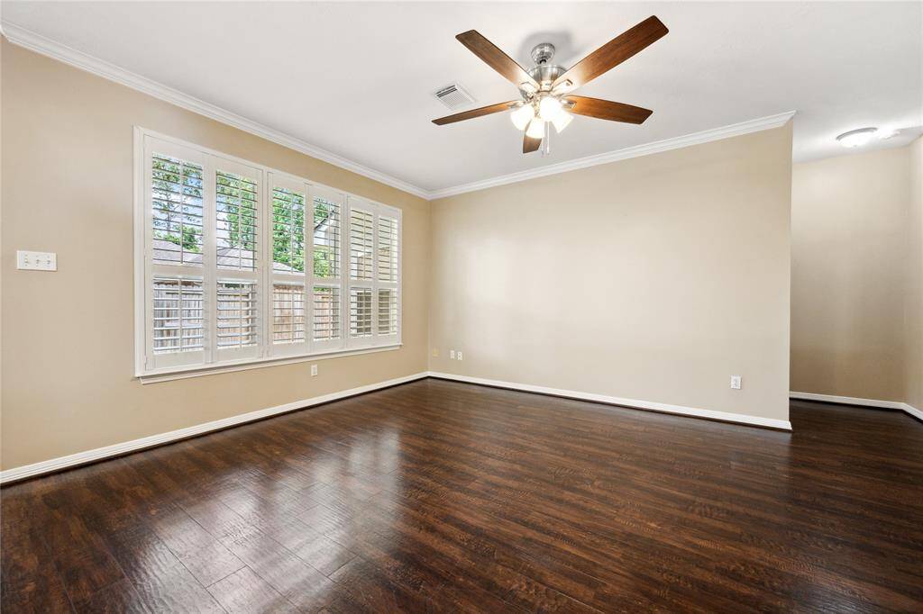 Bright and inviting room with wood floors, large windows with plantation shutters, and a ceiling fan. Neutral walls enhance the spacious feel. Ideal for a cozy living area.