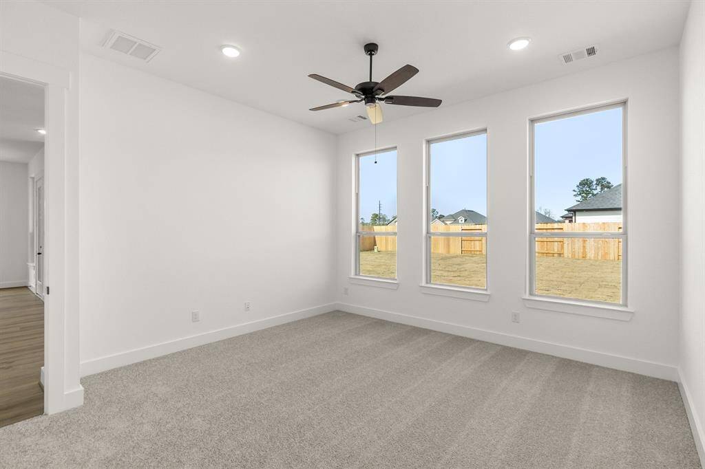 As you enter the primary bedroom, you’re greeted by an abundance of natural light pouring in through large, beautifully framed windows, casting a warm glow on the soft, neutral tones of the walls.