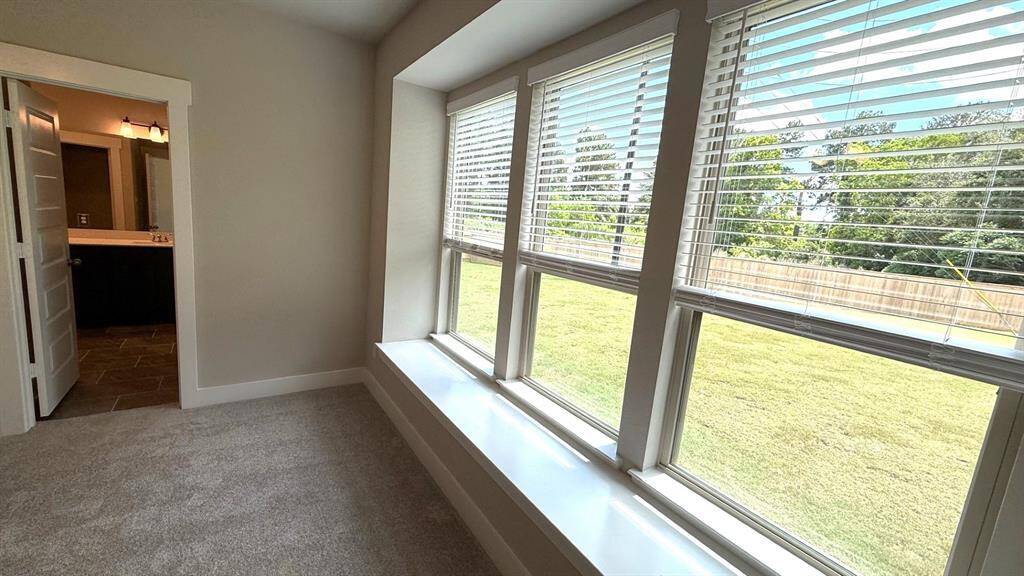 As you enter the primary bedroom, you’re greeted by an abundance of natural light pouring in through large, beautifully framed windows, casting a warm glow on the soft, neutral tones of the walls.