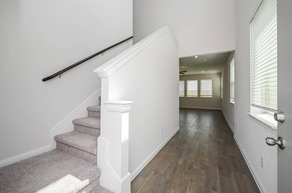 Snow white walls embrace good looking 'blond' wood-look tile? laminate? flooring, complemented by wide picture windows, in this inside view of the front entrance, with the convenience of the carpeted staircase at the entrance.